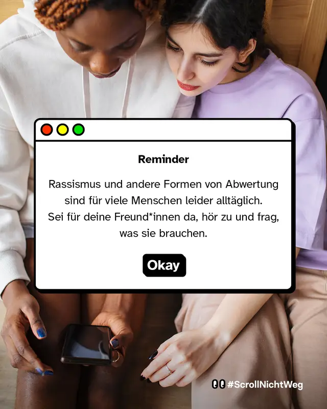 Zwei Personen sitzen nah beieinander und schauen gemeinsam auf ein Smartphone. Davor ein Fenster-Design mit Text: &bdquo;Reminder &mdash; Rassismus und andere Formen von Abwertung sind f&uuml;r viele Menschen leider allt&auml;glich. Sei f&uuml;r deine Freund*innen da, h&ouml;r zu und frag, was sie brauchen.&ldquo; Darunter ein Button mit &bdquo;Okay&ldquo;.